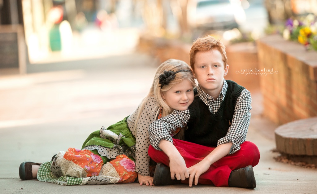 Brother and Sister sitting together for portrait on the sidewalk in downtown Belmont, NC
