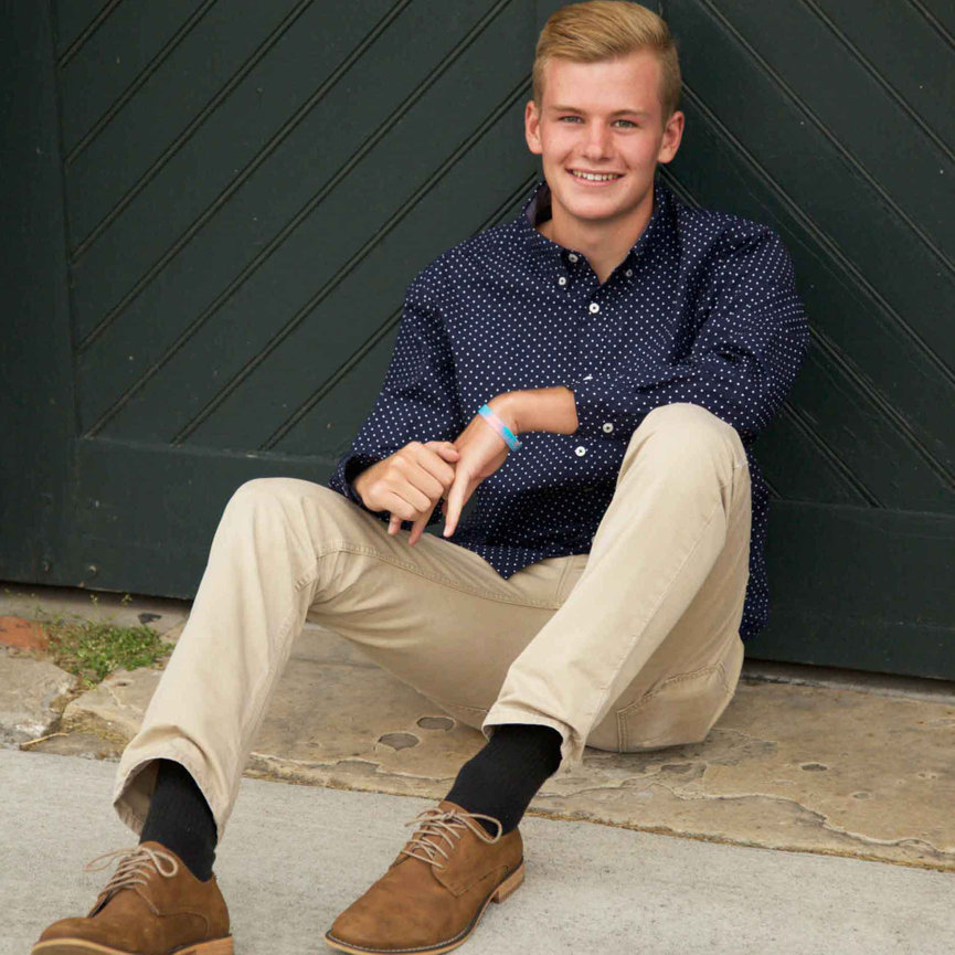 High school senior boy sitting confidently in front of a green barn door during an outdoor portrait session. Captured to showcase rustic charm, relaxed style, and timeless character. Luxury senior portrait experience for Colorado families