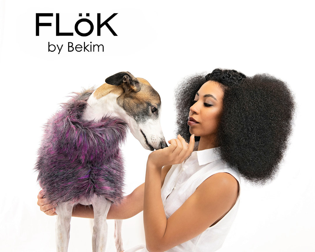 Woman with curly hair holds a dog in a purple fur outfit, featuring the brand name FLÖK by Bekim.