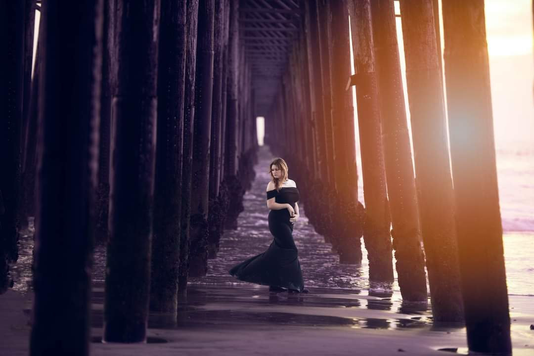Fine art maternity portrait under beach pier at sunset by Austin portrait photographer Texas Vogue Photography.
