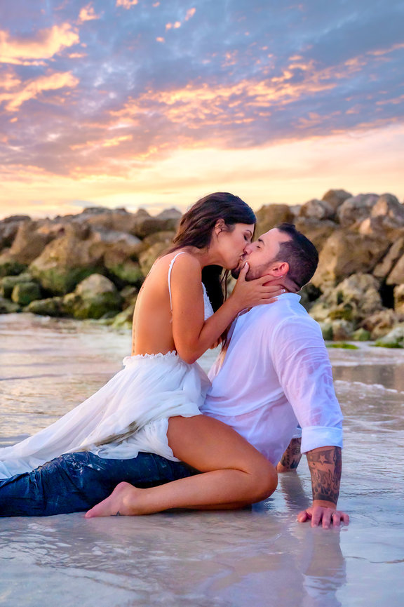 Couple embracing passionately on the beach at sunset, with waves gently lapping around them.