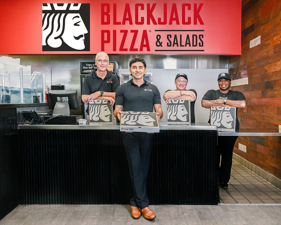 Four employees proudly display pizza boxes at Blackjack Pizza & Salads, with the restaurant's logo in the background.