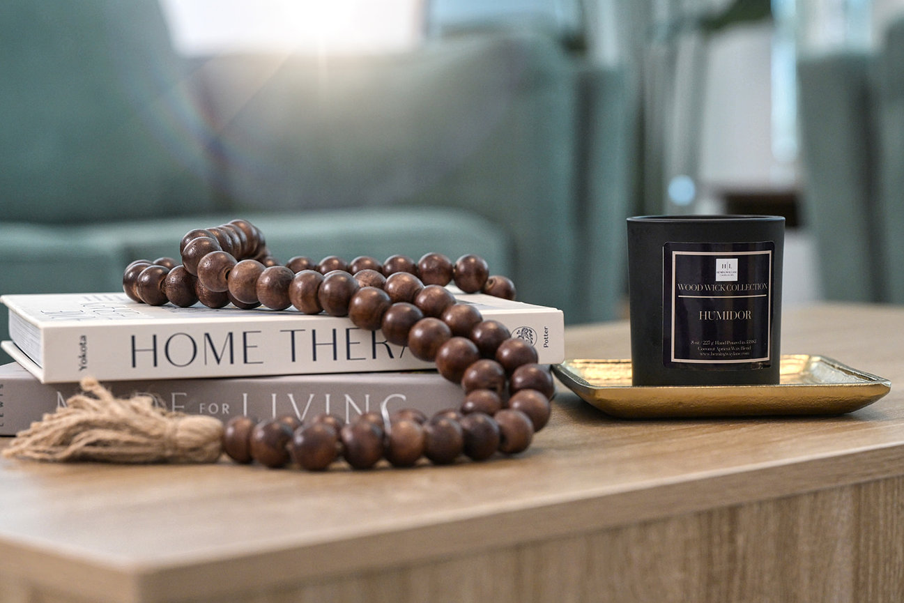 Wooden prayer beads on stacked books with a candle and decorative tray on a coffee table.