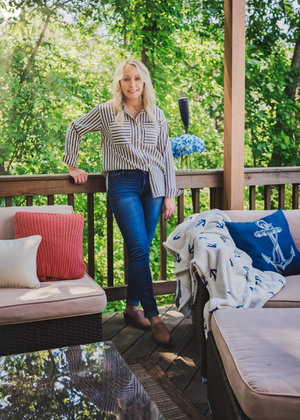 Woman standing on a deck, surrounded by outdoor furniture and greenery.