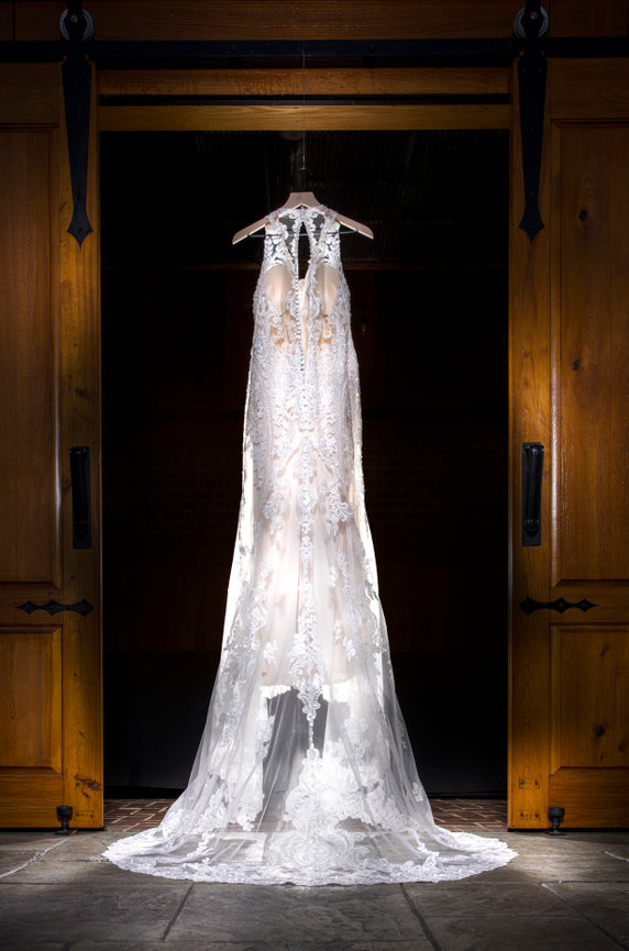 Lace wedding gown hanging in a barn doorway, illuminated by natural light before the ceremony at a rustic Alabama wedding venue. captured by gulf coast wedding photographer Dixon Creative Images