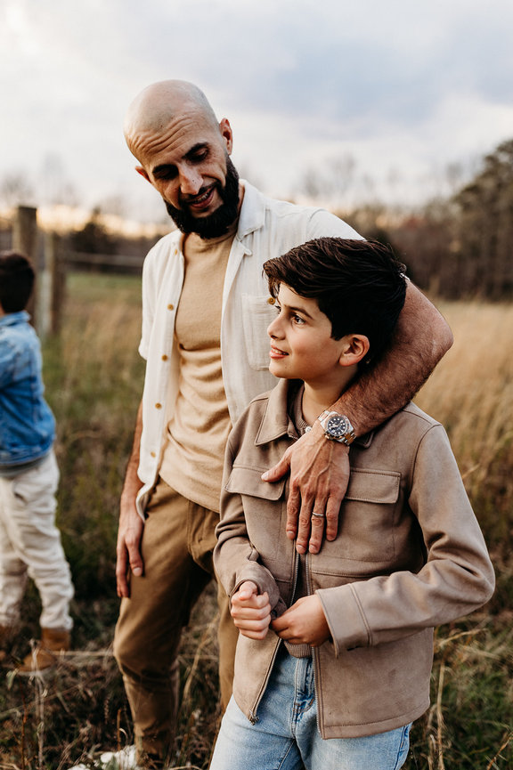 a father puts his arm around his son in a sunlit field during a Huntsville, Alabama family photoshoot
