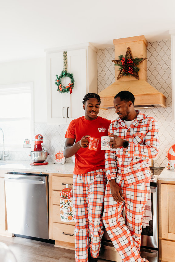 A father and son in holiday pajamas holding festive mugs in a decorated kitchen