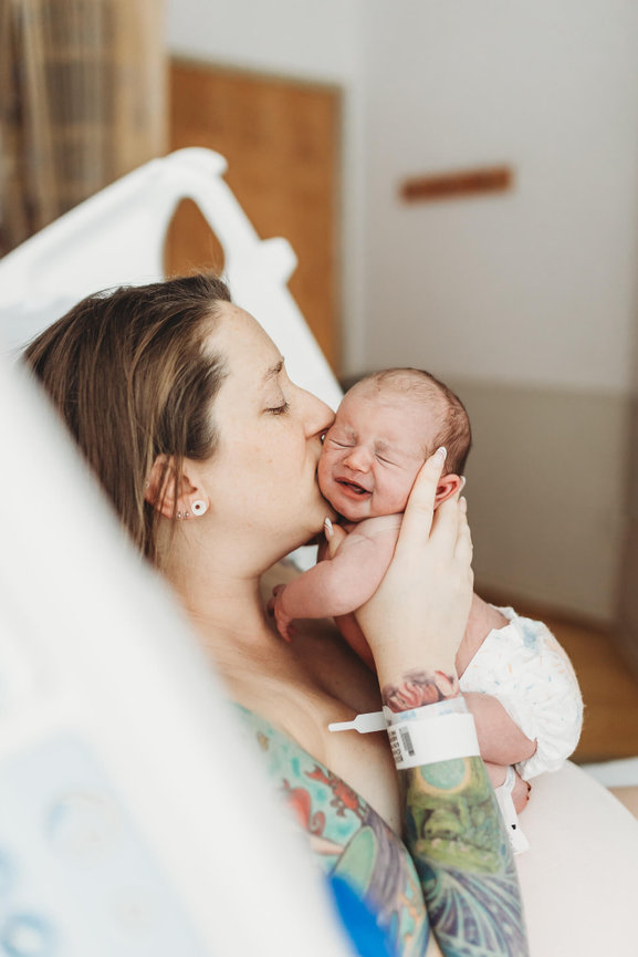 A mother kisses her newborn on the cheek while sitting in a hospital bed at Morristown Medical Center, New Jersey.