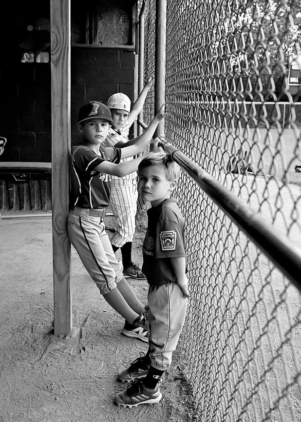 three brothers hand on the chain link fence in the baseball dugout