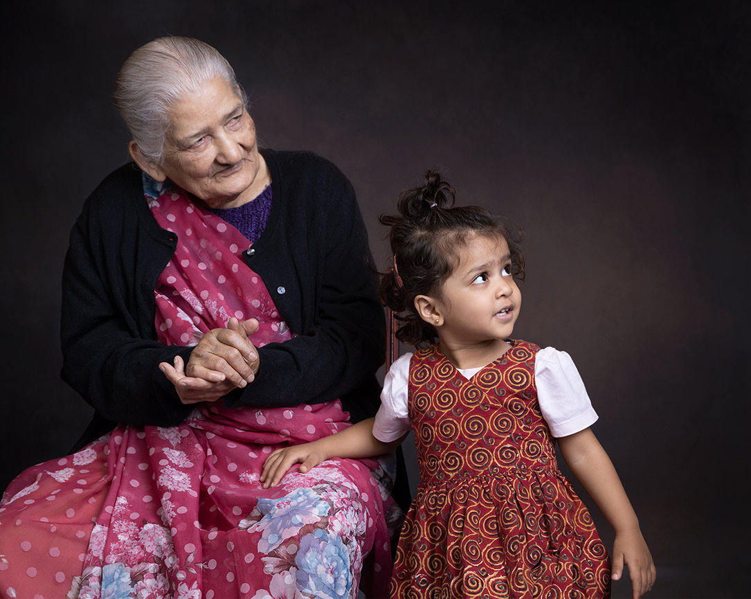 Fine art indoor portrait of a grandmother and great-granddaughter together in Carmel, Indiana, captured in soft light with a timeless multi-generational connection and expressive presence