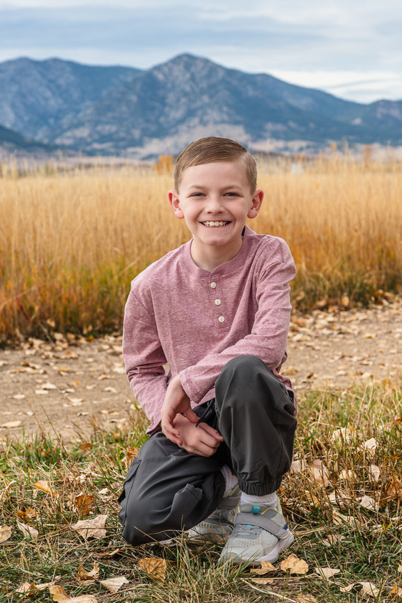 A young boy crouches in the grasses. The Colorado Rocky Mountains are framed behind him.