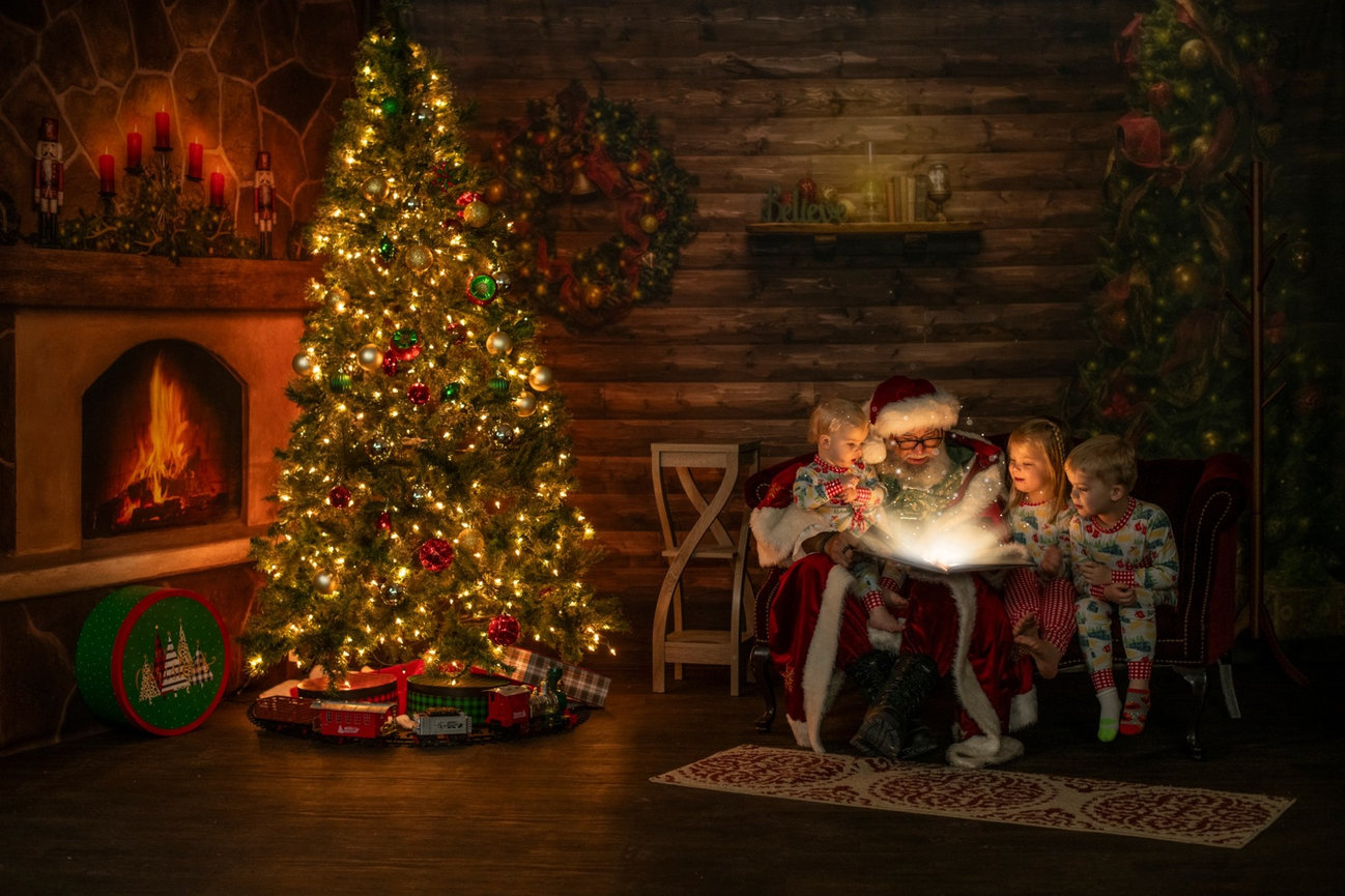Children gathered with Santa around a glowing storybook beside the Christmas tree