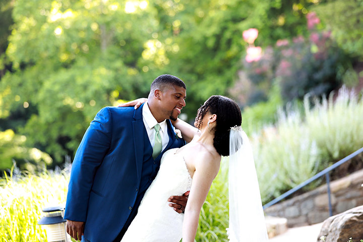 A couple in wedding attire smiling at each other in a garden setting.