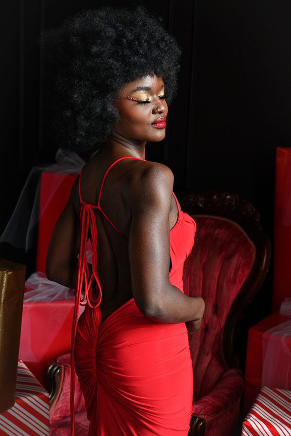 Elegant African American woman in a stunning red dress, posing confidently amidst festive red and gold decor in Salt Lake City, Utah. Captured by Tre Nelson Photography, showcasing grace and holiday glamour.