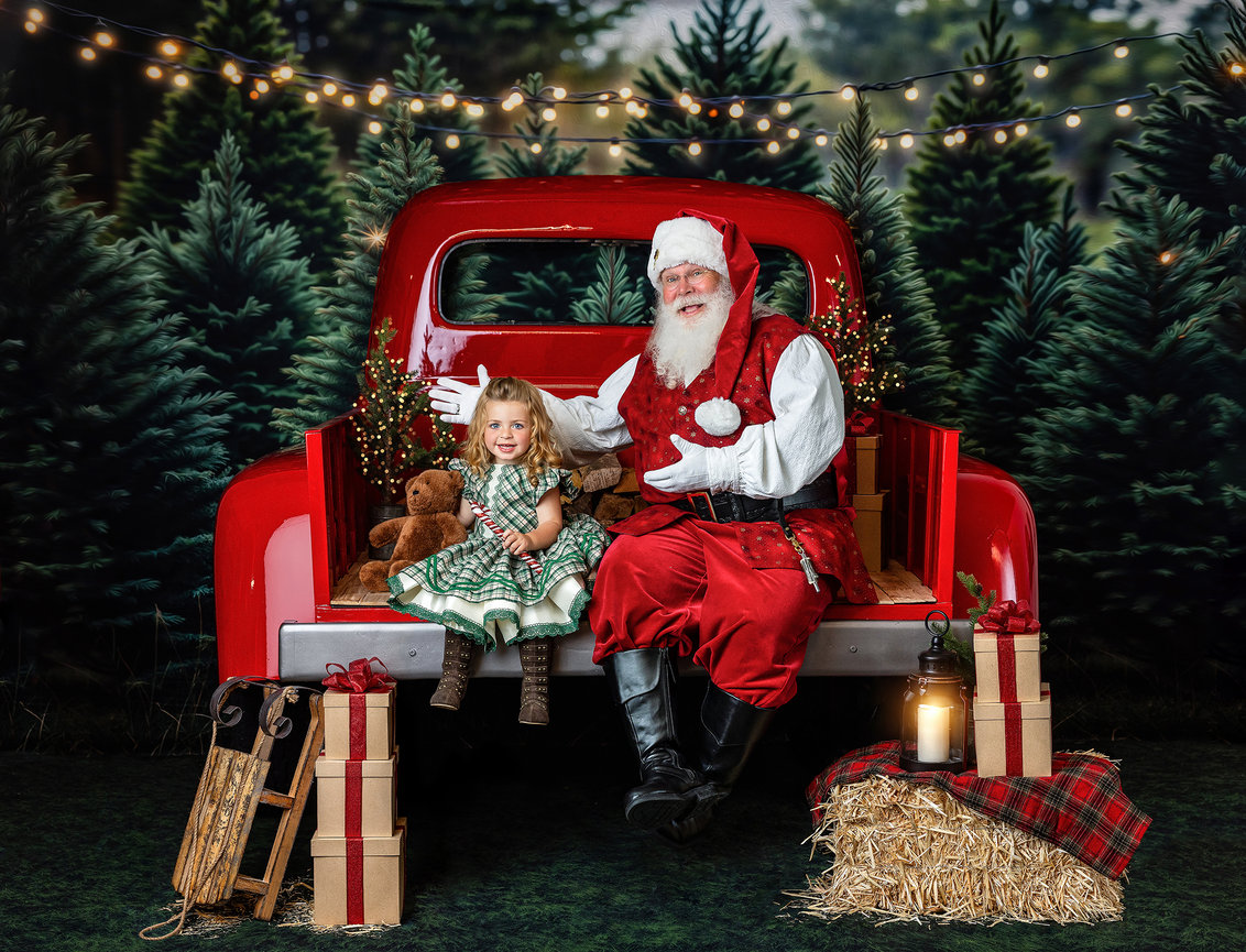 Santa Claus and child sitting in a vintage red Christmas truck surrounded by Christmas trees at a Santa Experience in Wooster, Ohio