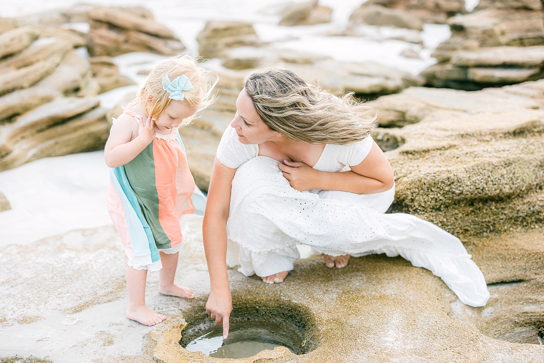 woman kneeling with little girl in pastel dress on the beach