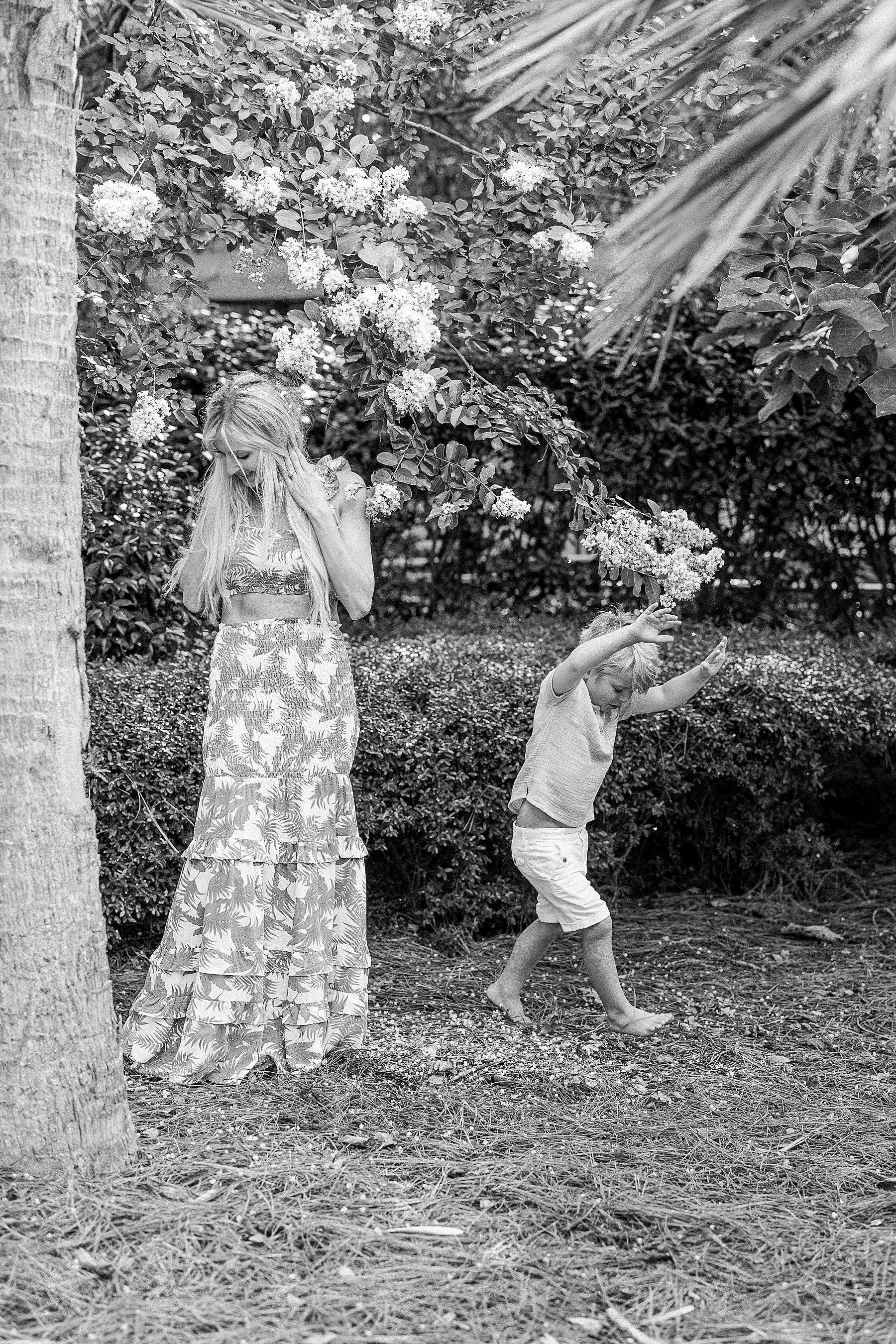 little boy dancing around mom in falling white flowers wearing brown shirt and white shorts