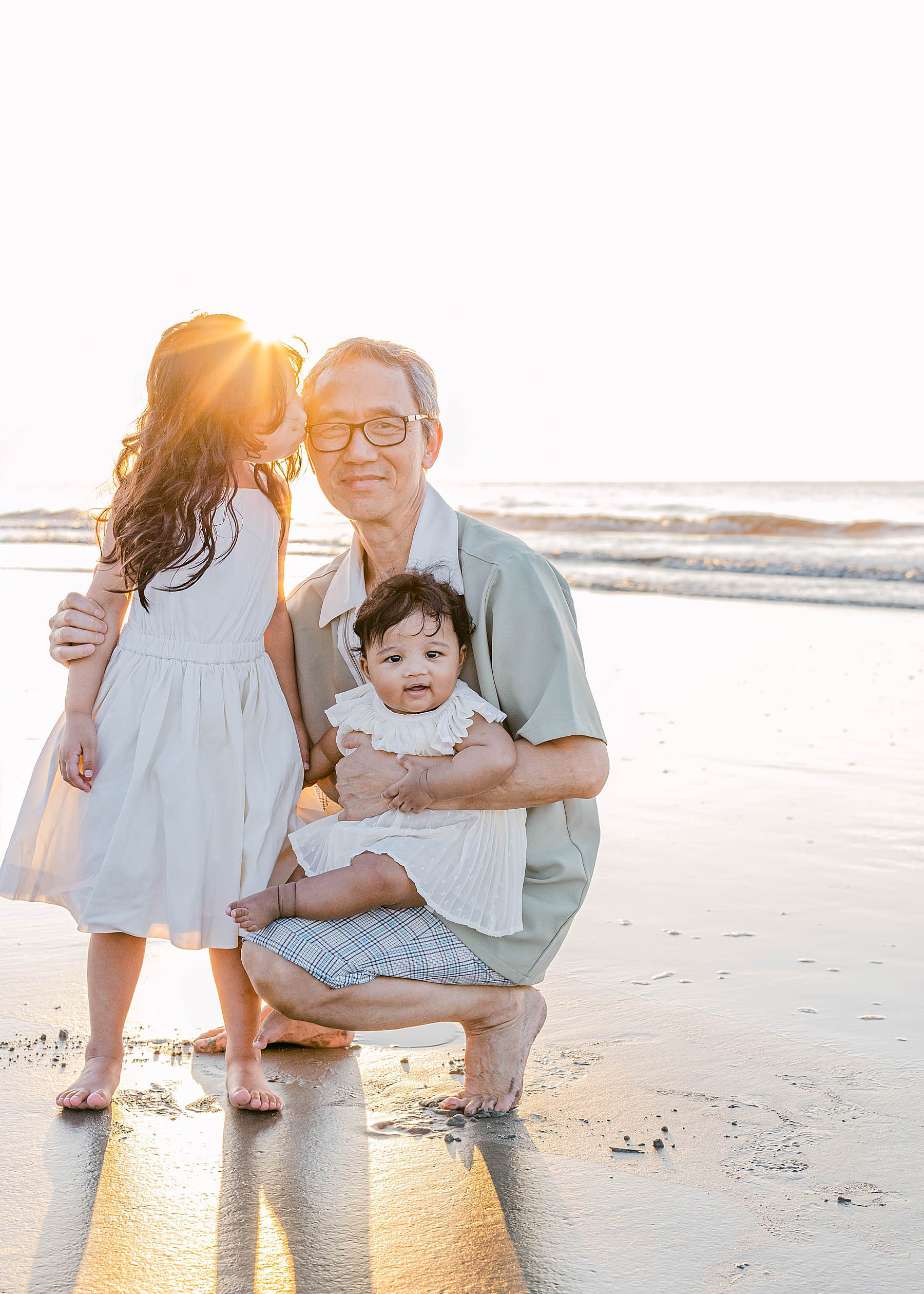 old man with grandchildren kneeling hugging them on the beach