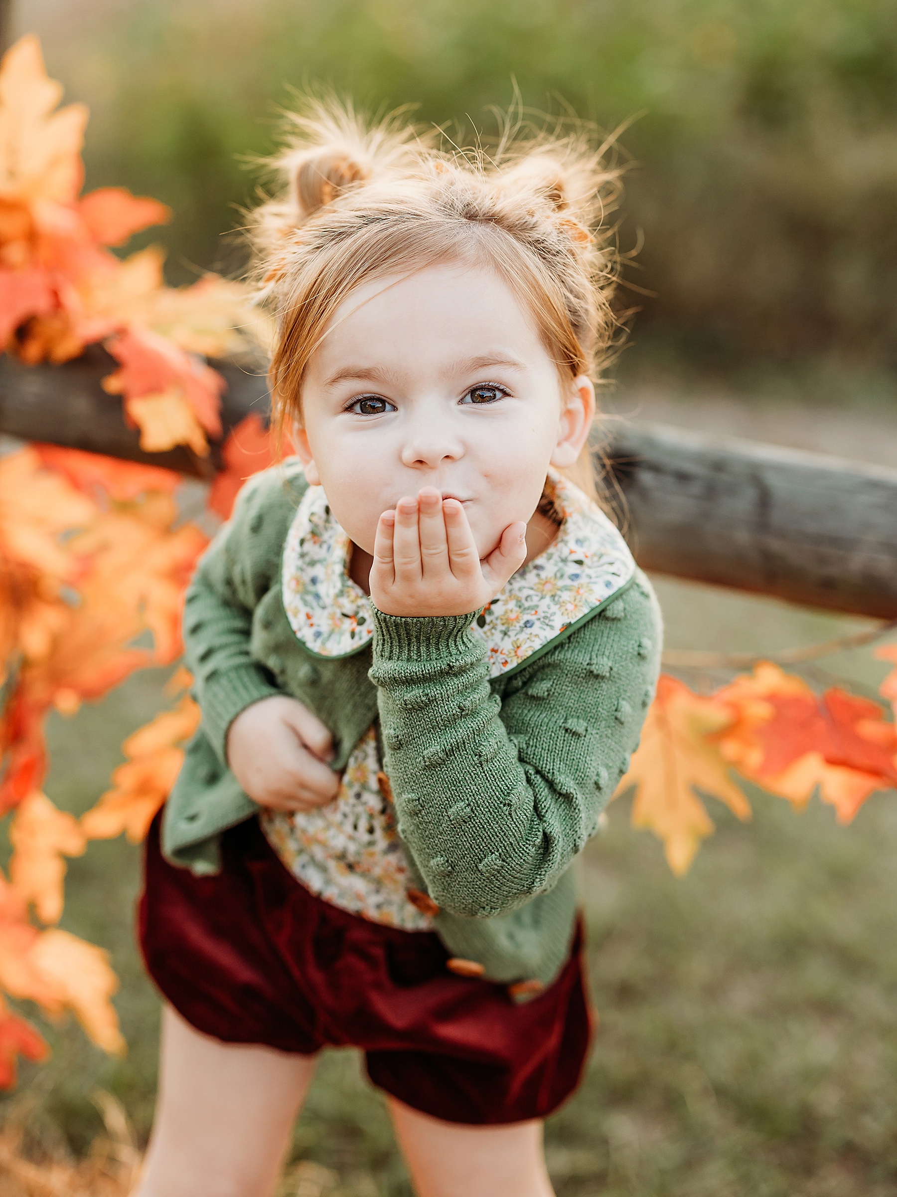 little girl in green sweater blowing a kiss at the camera