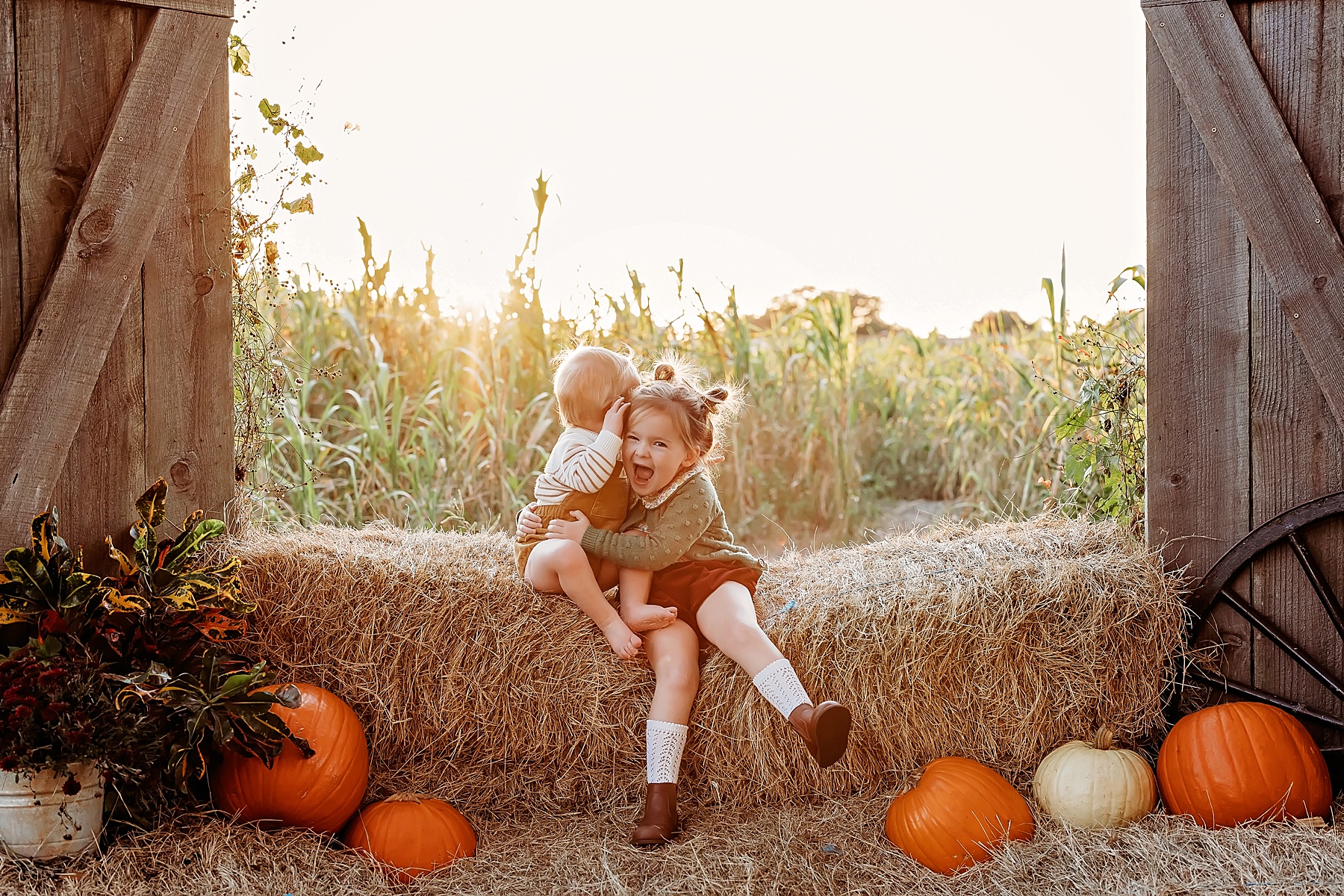 girl wearing green sweater sitting with baby boy on bales of hall in the fall