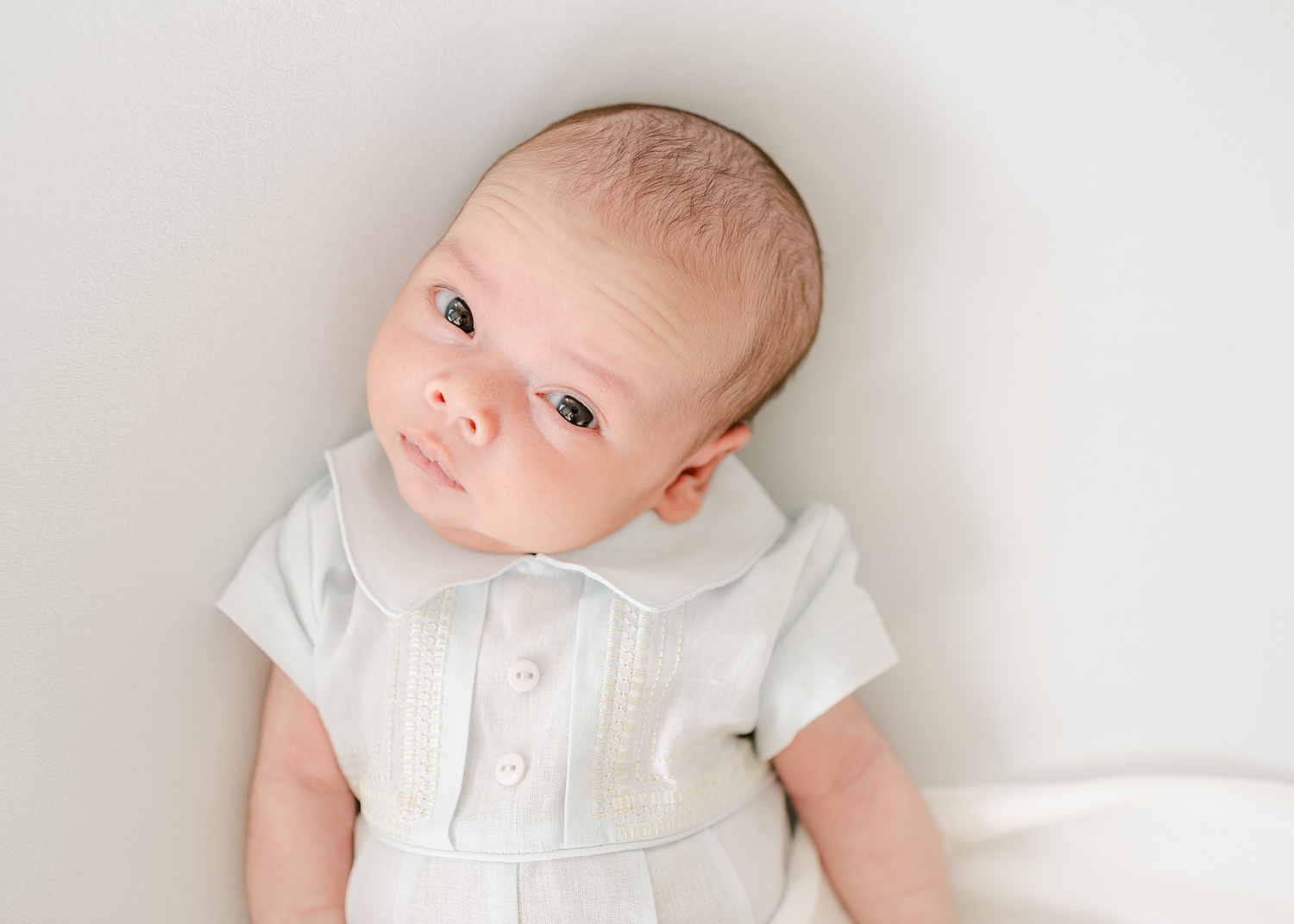 newborn baby boy dressed in pale blue heirloom outfit looking at camera
