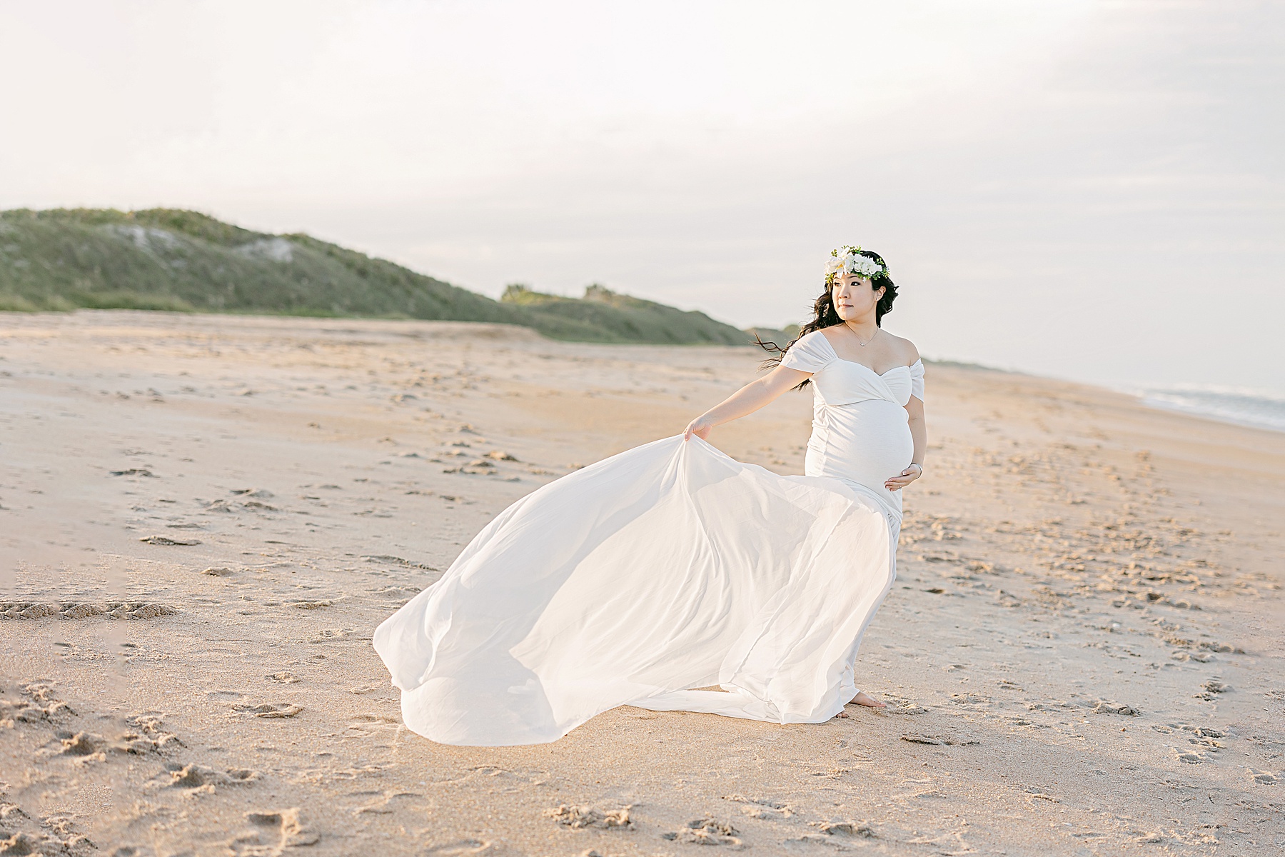 pregnant woman wearing long white dress on the beach with floral crown