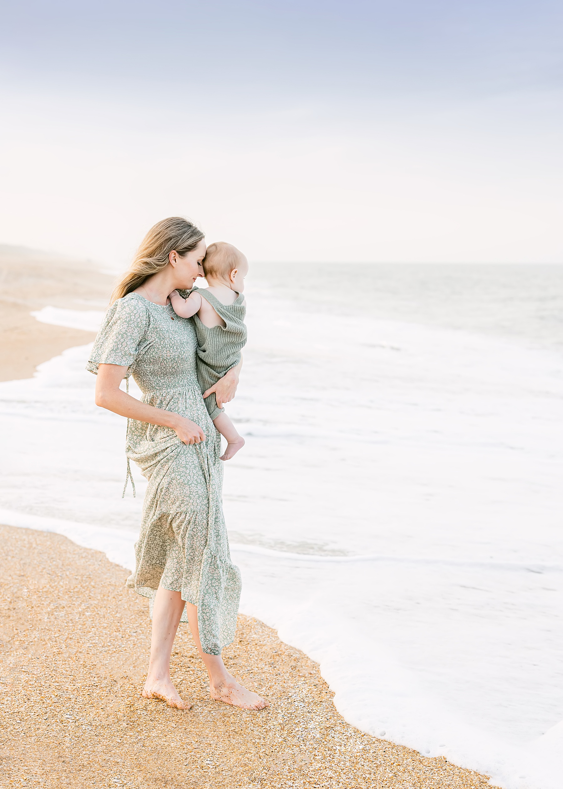 woman holding baby boy near the water on the beach wearing long green dress