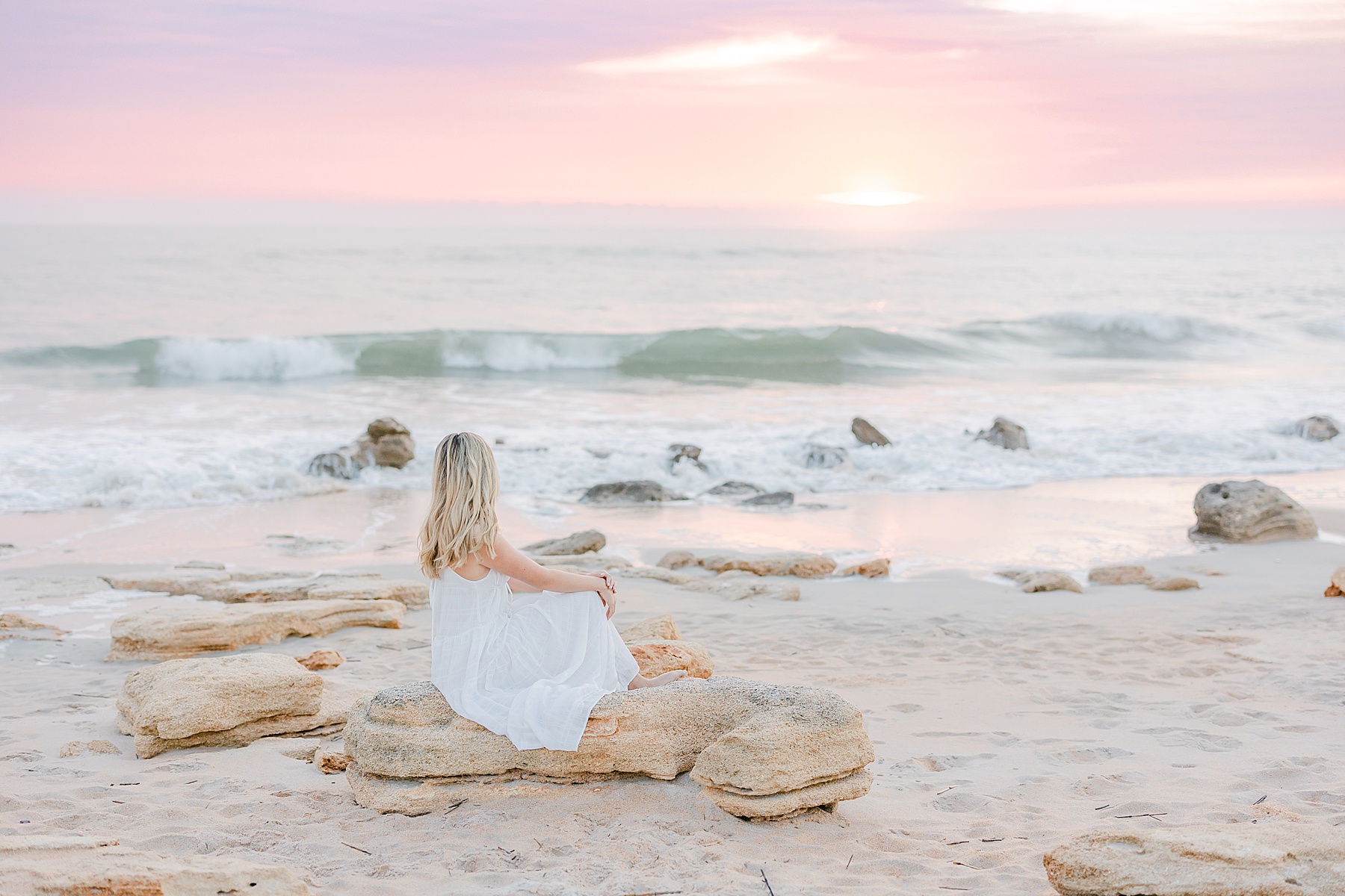 long white dress, st. augustine beach at sunrise, young woman sitting on the rocks at sunrise, pastel sky, florida sunrise, pastel colors, light and airy photograph