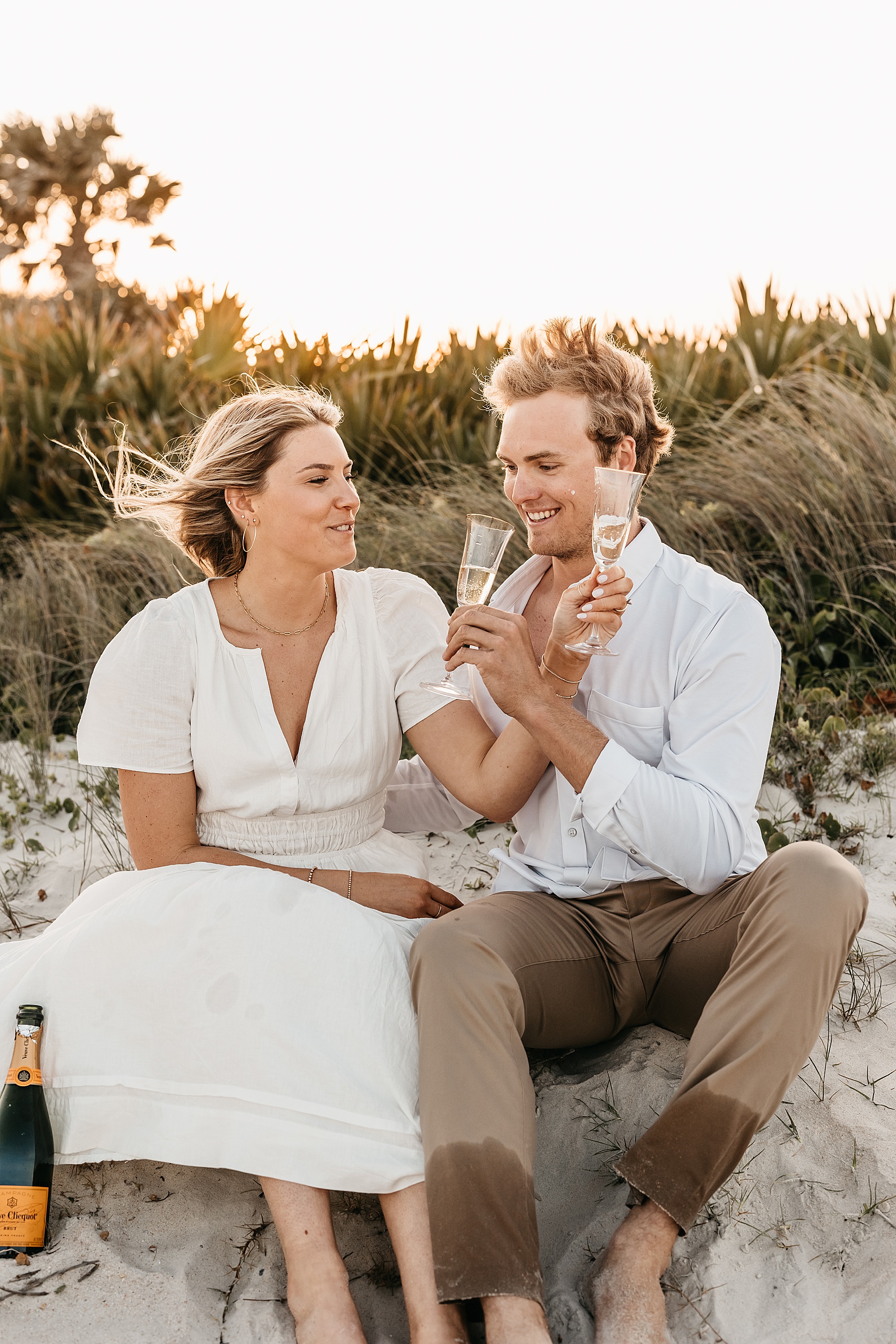 man and woman holding champagne glasses toasting on the sand