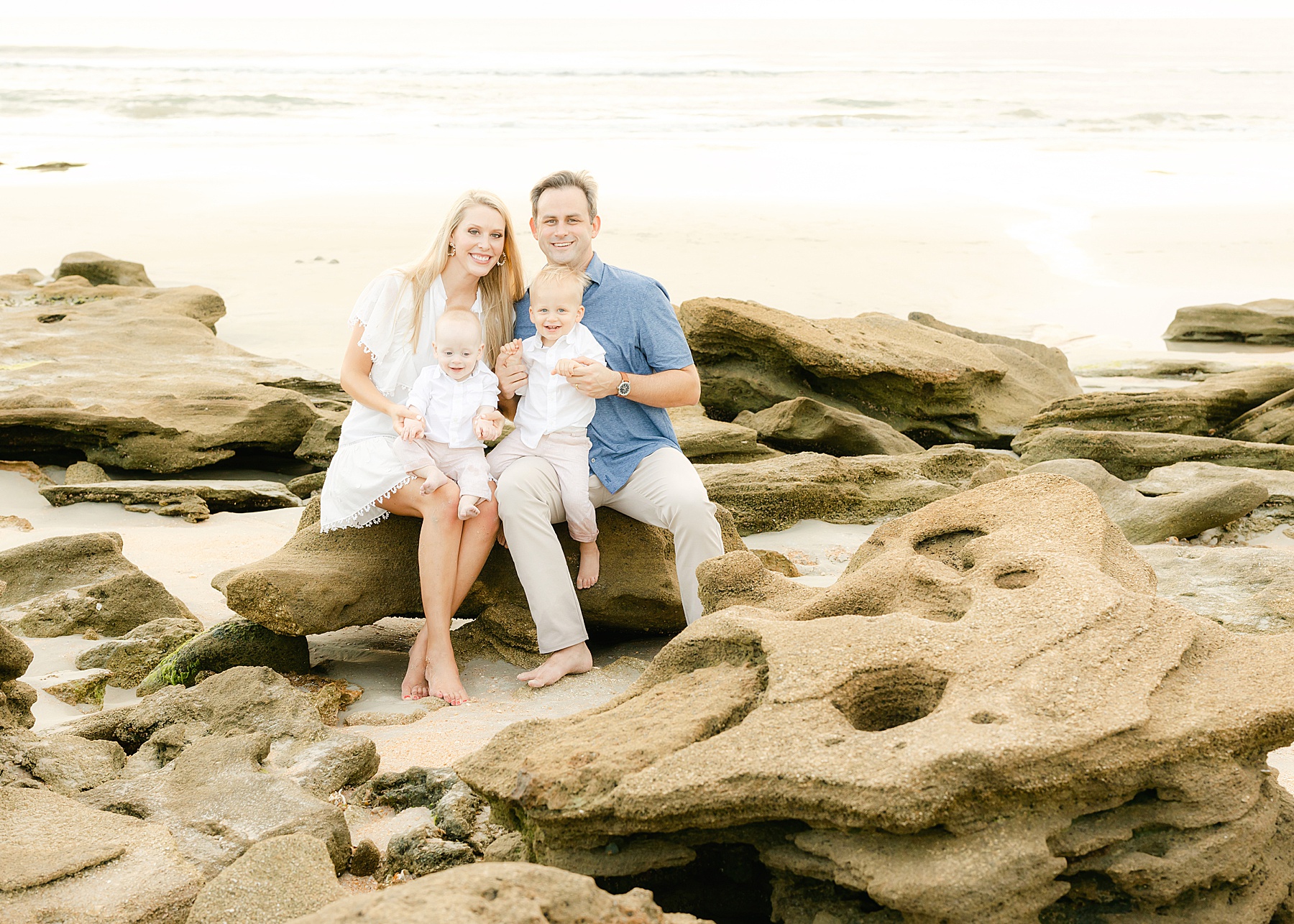 family of four sitting on the rocks on the beach in st. augustine florida light and airy sunrise family portrait