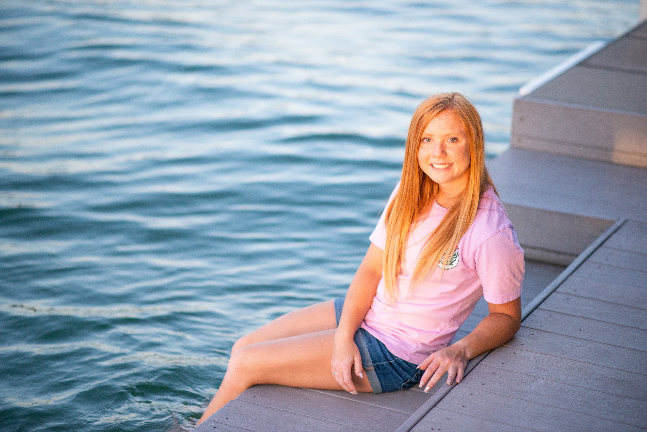 Senior girl wearing pink t-shirt sitting on a Tablerock Lake dock at sunset. 