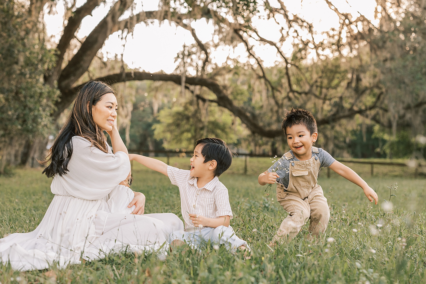 Asian woman in long white dress sitting in a flower field with two little boys