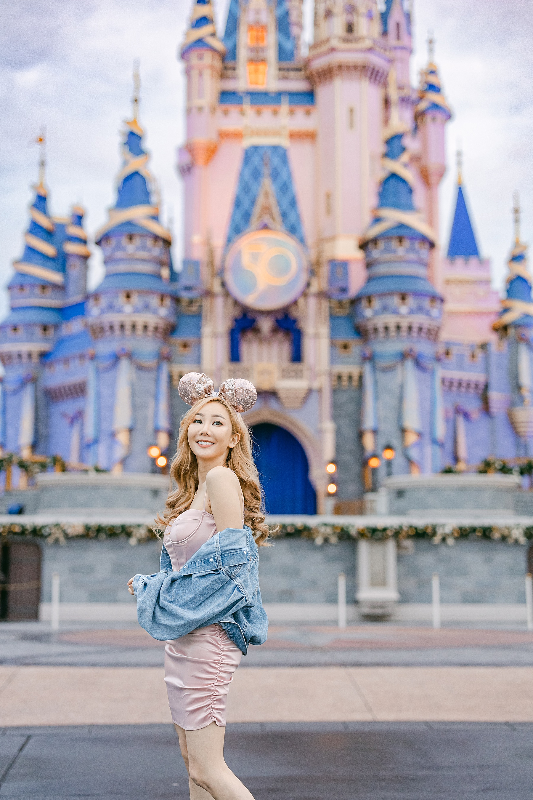 asian woman in fitted pink dress and jean jacket smiling in front of Cinderella's Castle