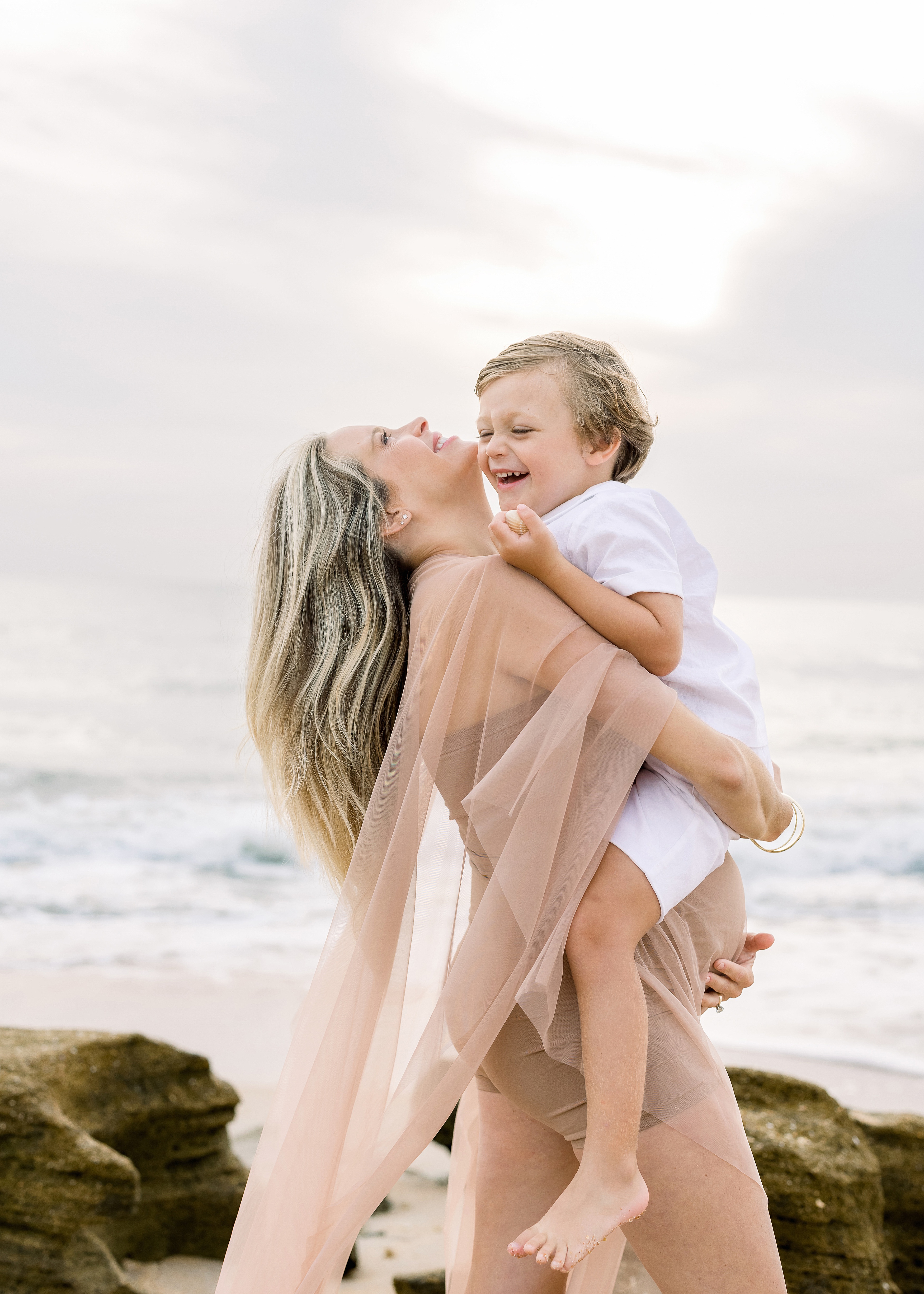 blond pregnant woman holding little boy dressed in white on the beach
