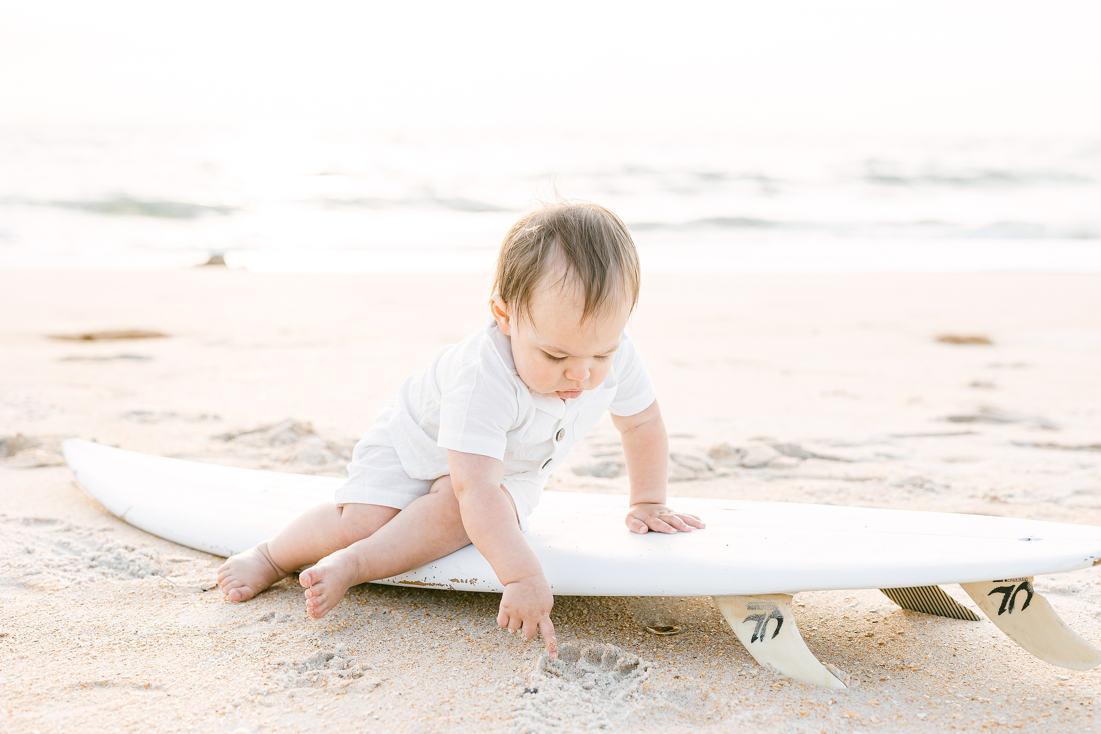 baby boy sitting on a white surfboard on the beach in St. Augustine