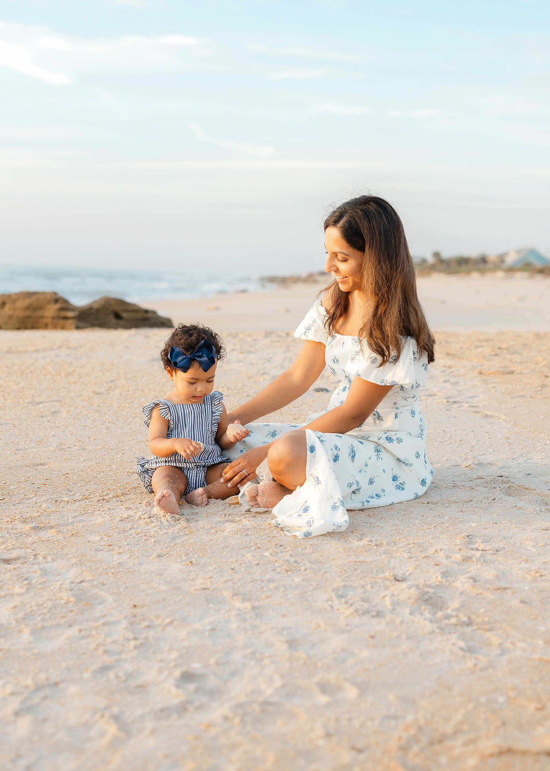 Woman sitting with baby girl on the sand at St. Augustine Beach at sunrise.