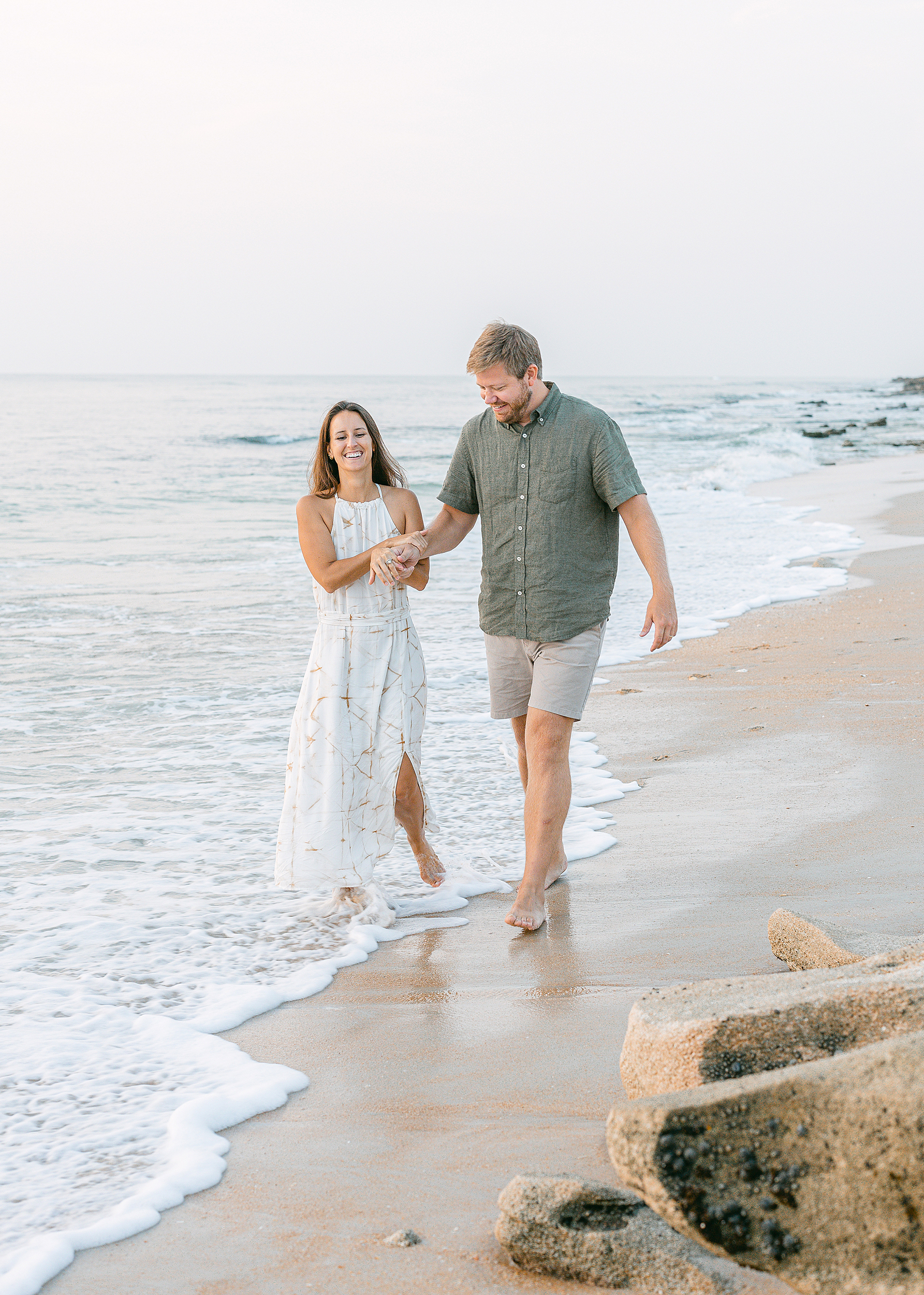 Man and woman walking down the shoreline together during a family beach portrait session at sunrise.