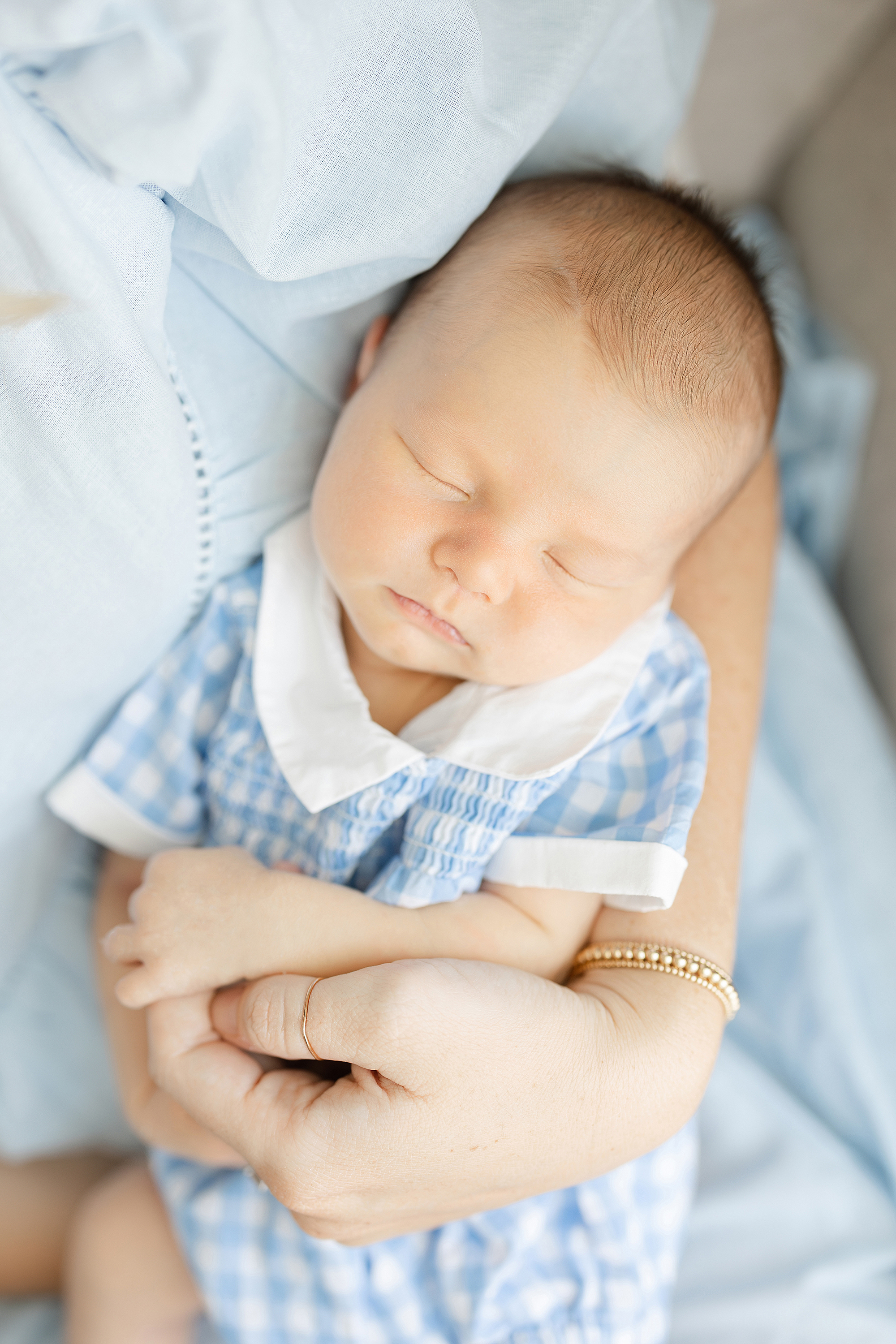 Newborn portrait of a baby boy dressed in blue and white checkered outfit.