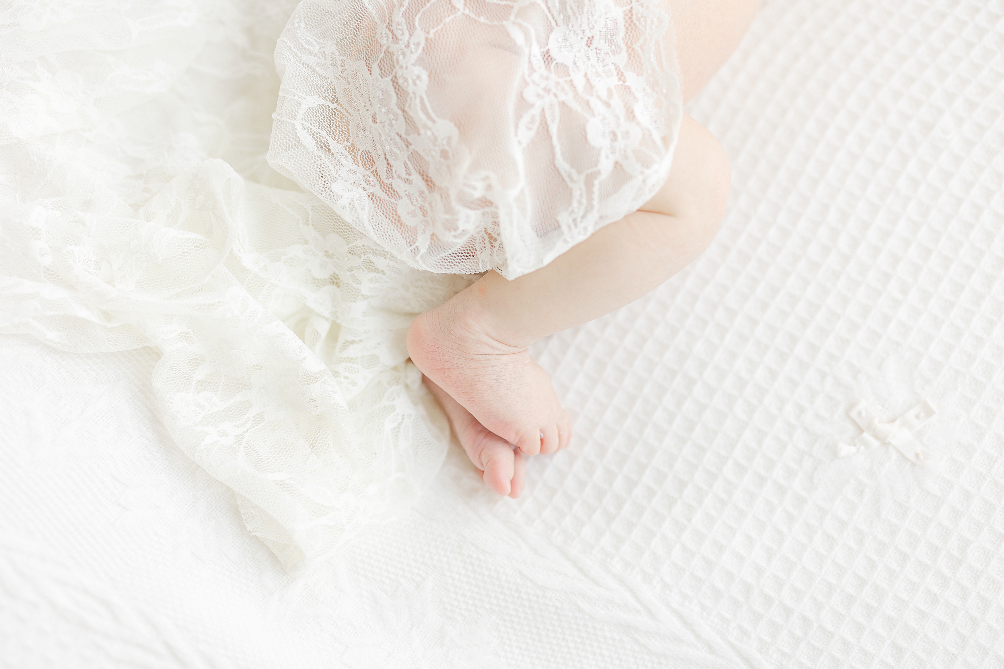 A newborn detail shot of a baby girl in a lace swaddle on a white bed.