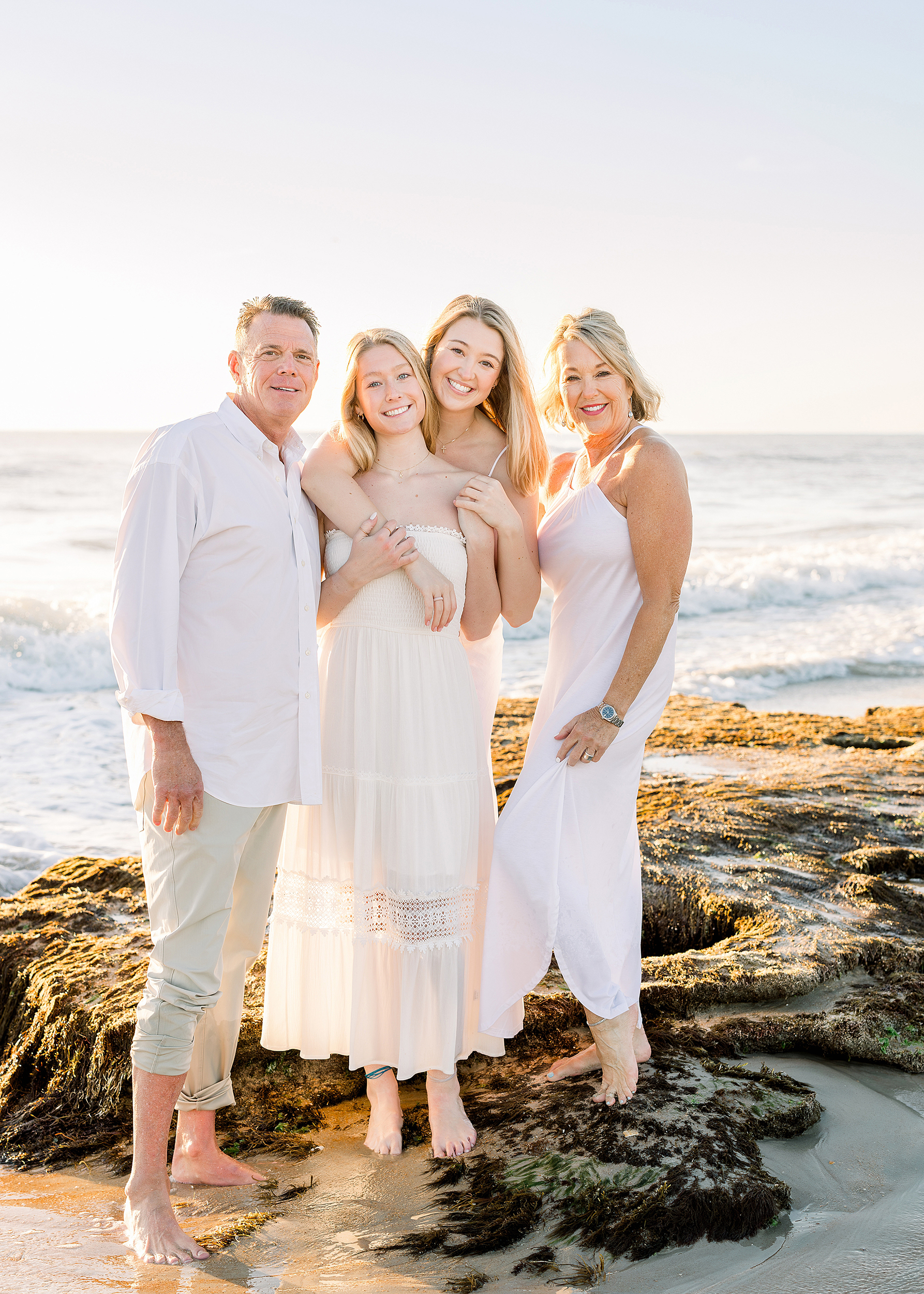 A sunrise portrait of a family of four standing on the rocks on the beach in Saint Augustine, Florida.