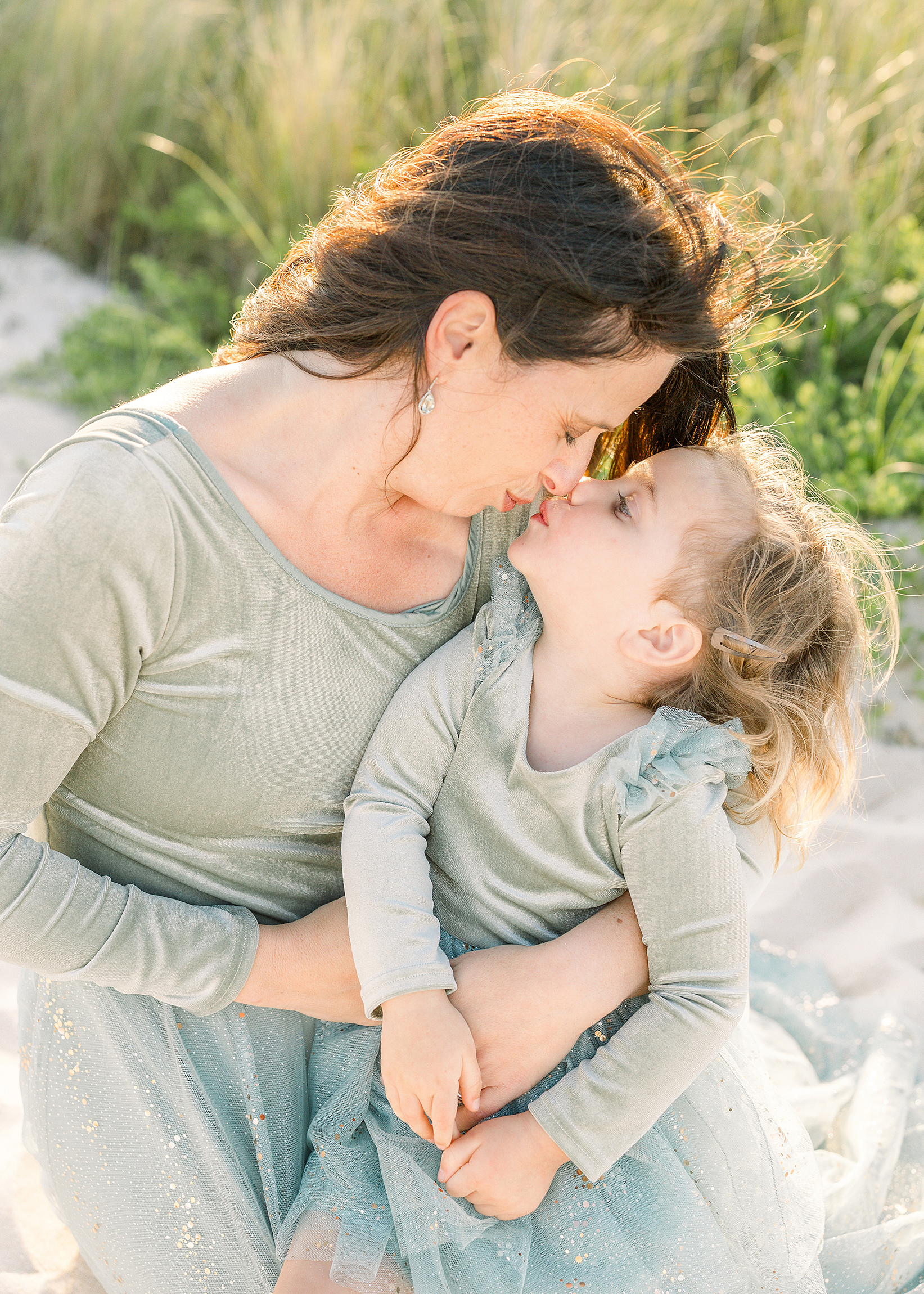 A mother and daughter kiss each other at sunset on the beach.