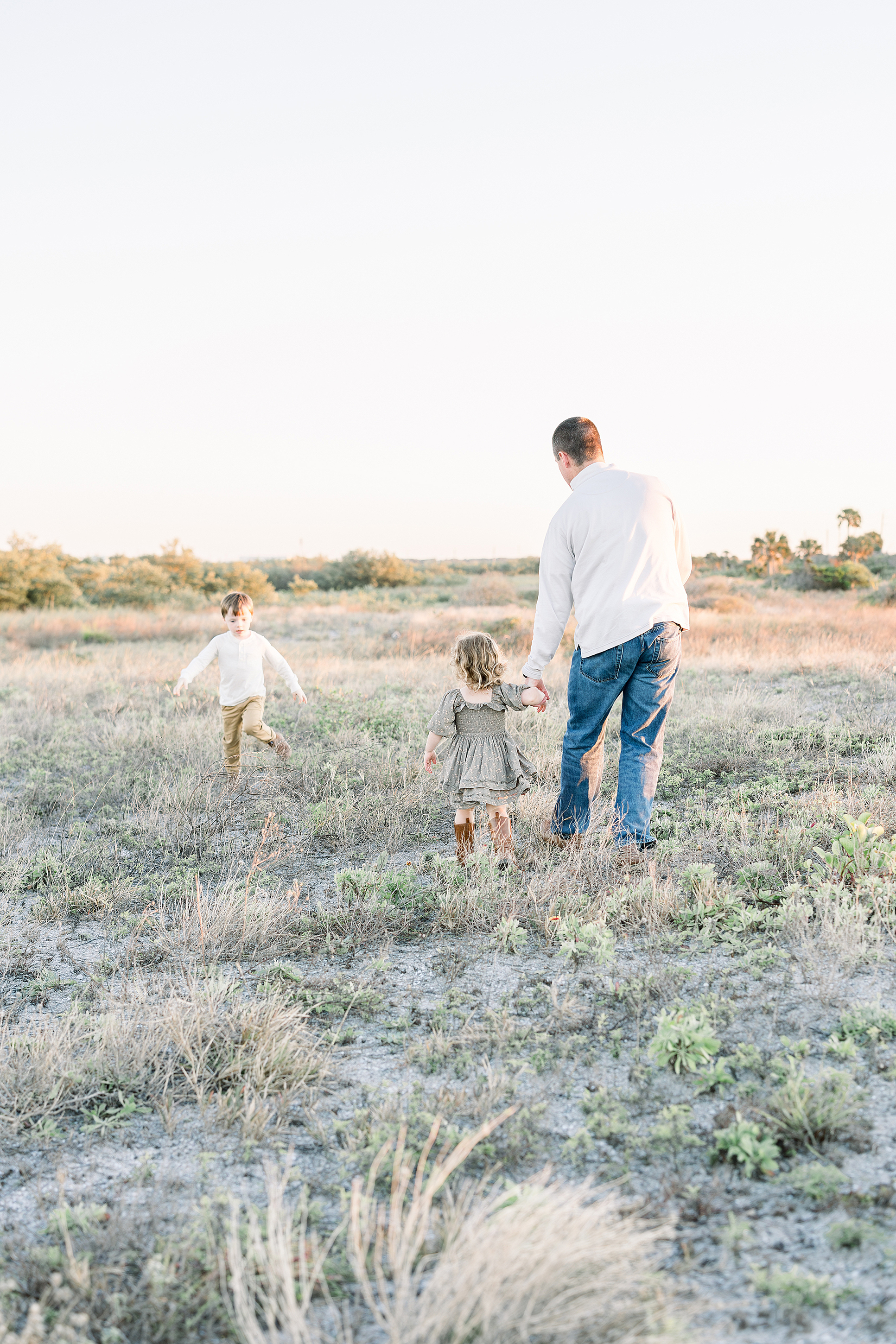 A family portrait of a father playing in the grassy field with his two little children.