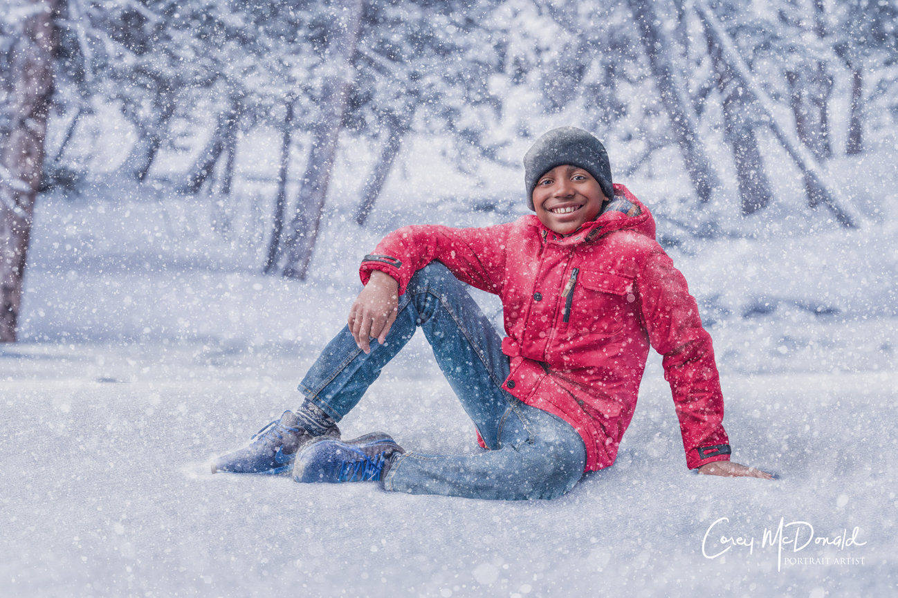 A child in a red coat and beanie sits smiling in a snowy forest, surrounded by falling snowflakes.