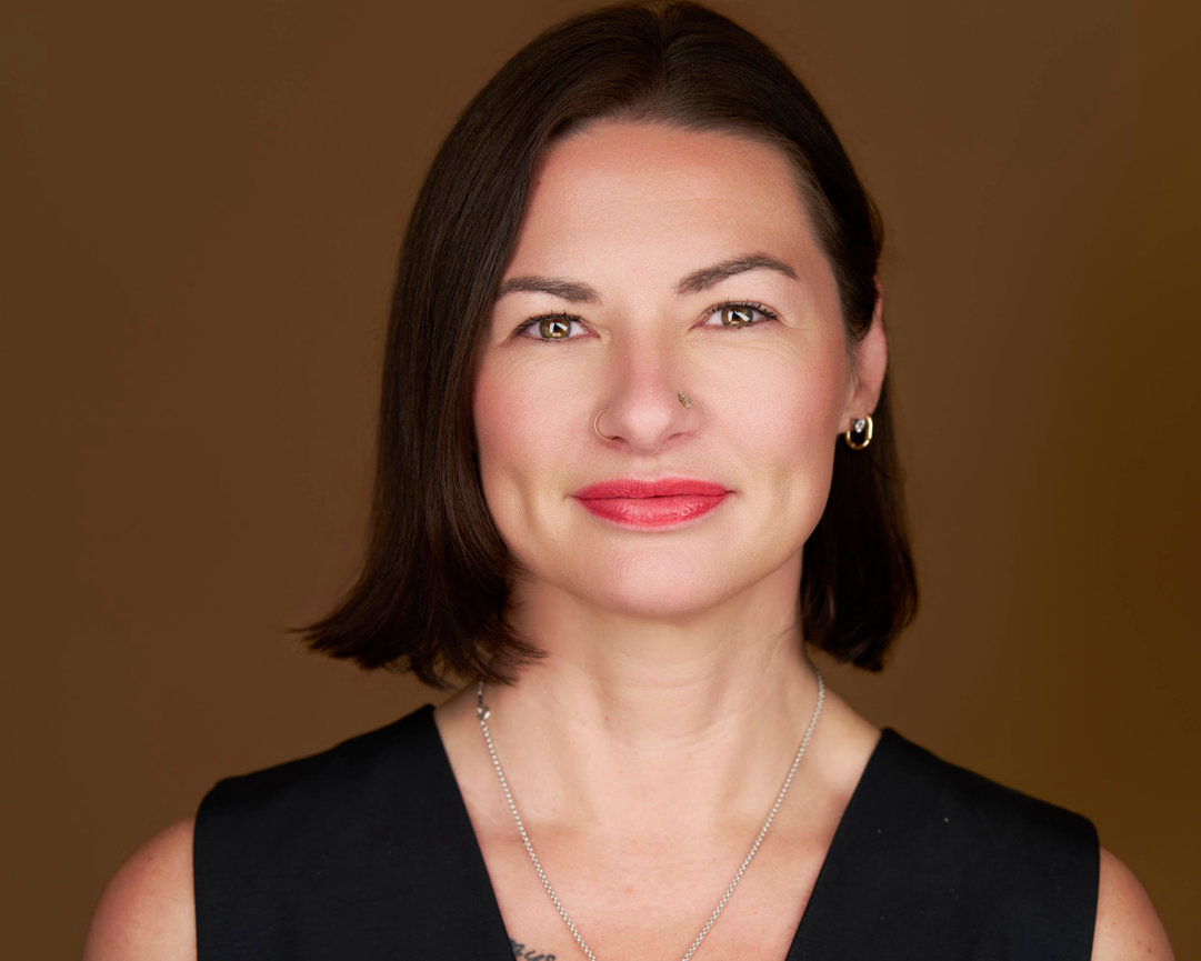 Portrait of a woman with short dark hair, red lipstick, and a black sleeveless top against a brown background