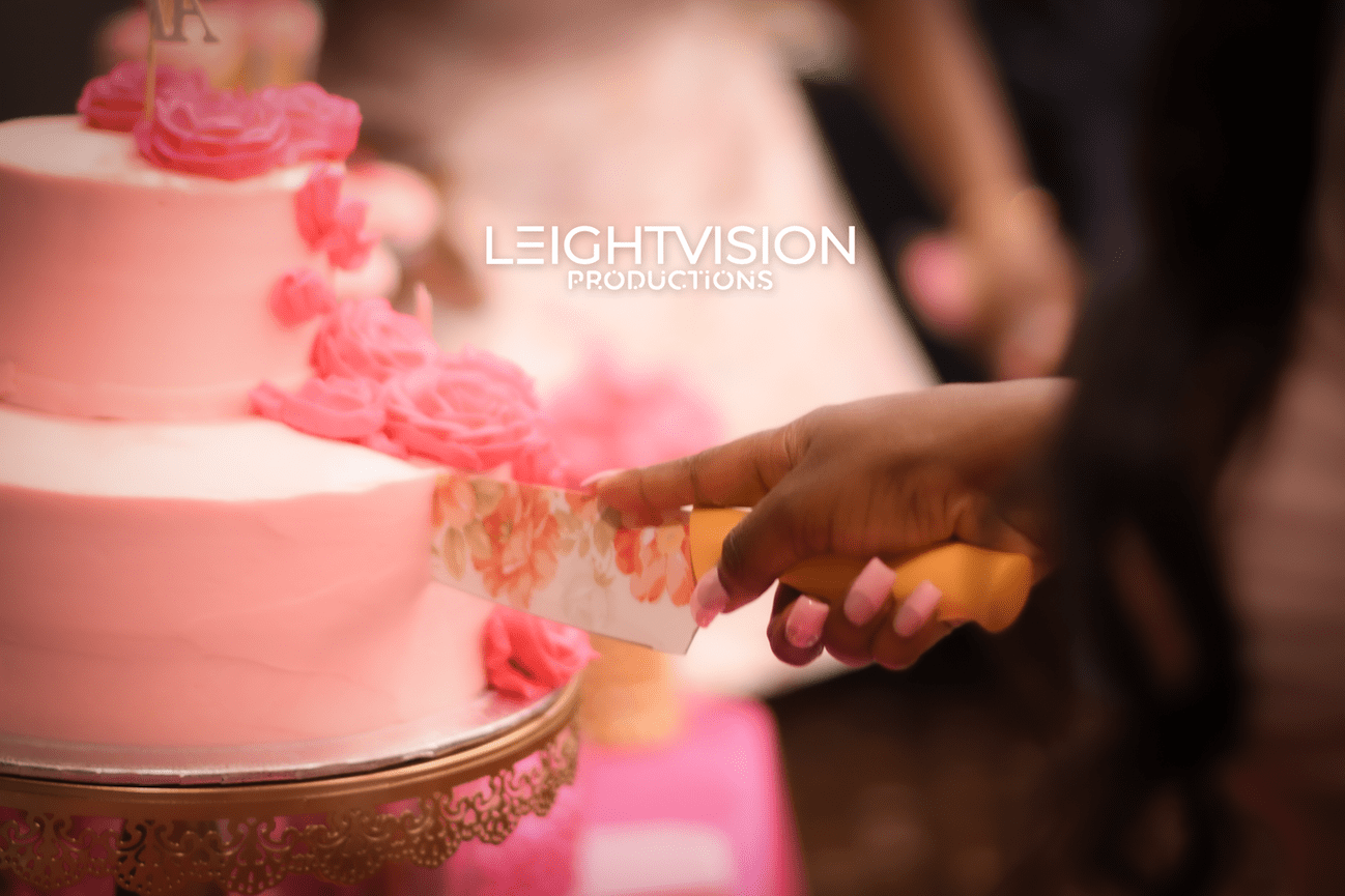 A person is cutting a beautifully decorated cake with pink icing, capturing a celebratory atmosphere.