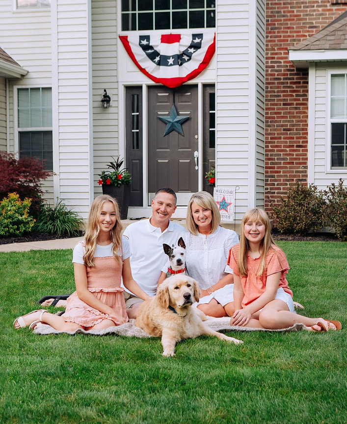 Family portrait with dogs sitting in grass in front of house in summer