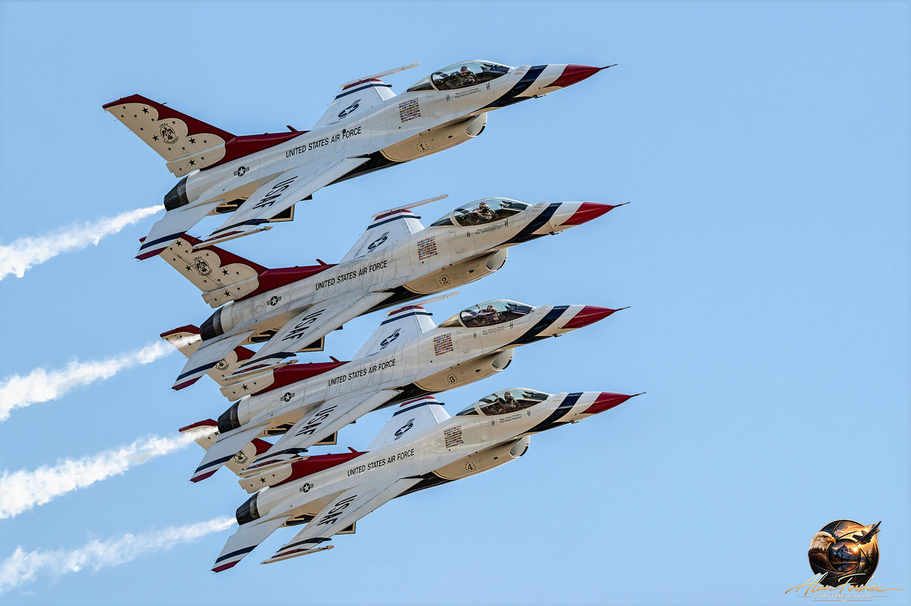 Four U.S. Air Force Thunderbirds F-16 fighter jets flying in tight formation with white smoke trails against a blue sky.