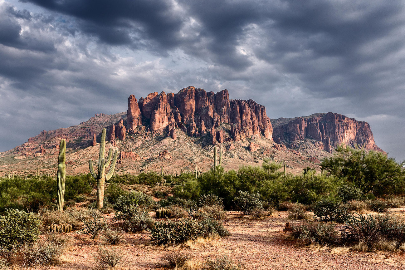 Fine art desert landscape featuring the Superstition Mountains, towering rock formations, saguaro cacti, and dramatic clouds.