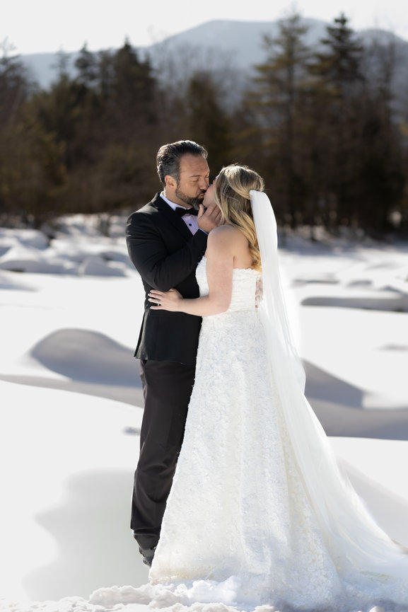 An intimate kiss between a bride and groom during a snowy New Hampshire winter wedding; featuring the panoramic White Mountains in the background and a cinematic, fine-art approach to destination elopement photography.