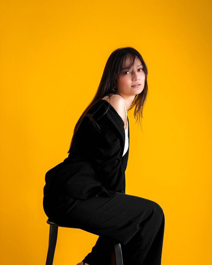 Woman in dark outfit on yellow background